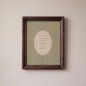 May include: A framed print with a dark brown wooden frame. The print features a green and white gingham pattern background with an oval-shaped text overlay. The text reads, "When my heart is overwhelmed, lead me to the rock that is higher than I." Psalm 61:2.