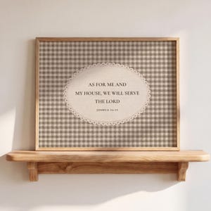 Op de afbeelding: Een rechthoekig ingelijst wandkunstwerk met een beige en bruine gingham-ruitjesachtergrond. In het midden staat een ovaal crèmekleurig label met een geschulpte rand en de tekst: AS FOR ME AND MY HOUSE, WE WILL SERVE THE LORD JOSHUA 24:15.