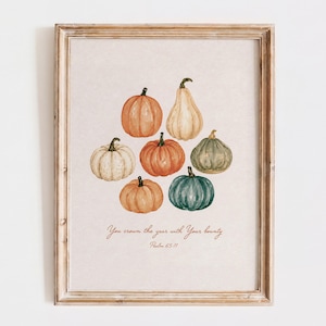 May include: A framed wall art print featuring a watercolor illustration of seven pumpkins in various shades of orange, white, green, and tan. Below the pumpkins, the text reads: You crown the year with Your bounty Psalm 65:11 in a brown script font.