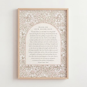 May include: A framed print with a prayer for marriage, set against a floral pattern in beige and pink. The text is within an arched design, and the frame is a light wood colour. The print is suitable for a home.