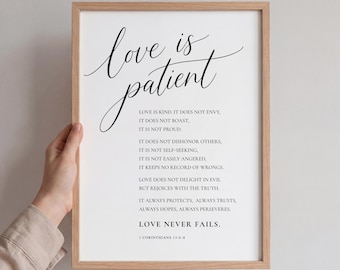 May include: A framed print with the words "love is patient" in elegant script. The print features a list of qualities of love, with the text "Love never fails" at the bottom. The frame is a light brown color.