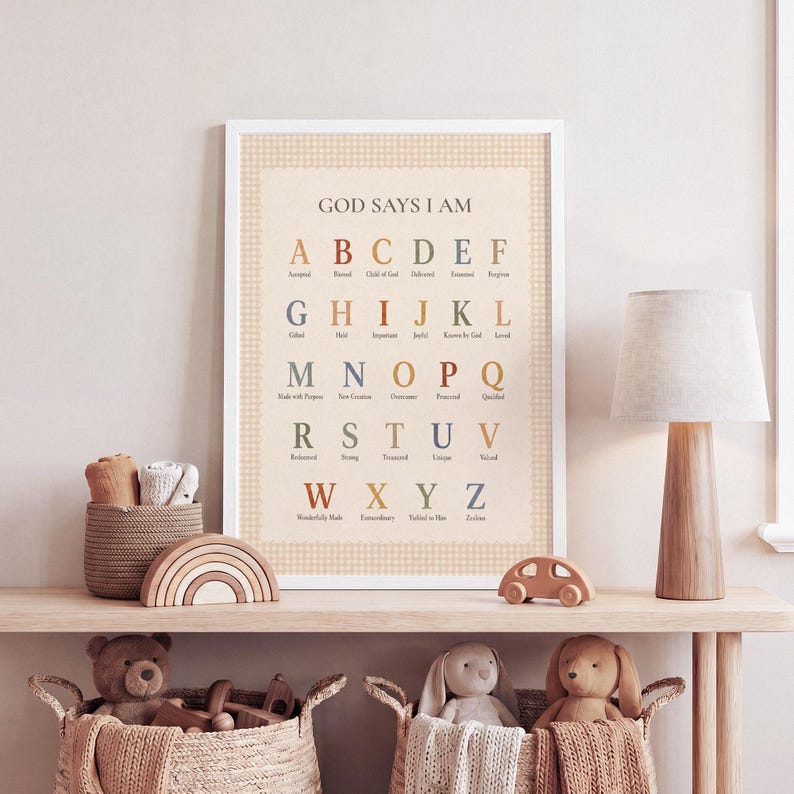 May include: A rectangular wall art print featuring the alphabet in a muted color palette with the text GOD SAYS I AM. Each letter is paired with a descriptive word like Accepted, Blessed, and Child of God, set against a light beige background.