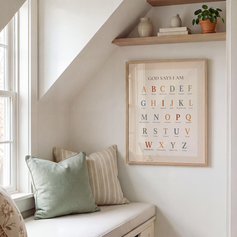May include: A framed wall art print titled GOD SAYS I AM featuring an alphabet from A to Z in various muted colors. Each letter is paired with a descriptive word, all set against a cream background with a subtle checkered border in a light wood frame.