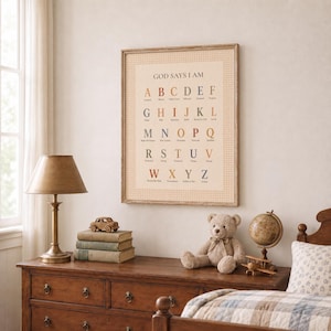 May include: A framed wall art print titled GOD SAYS I AM featuring an alphabet chart with each letter paired with a descriptive word in a muted color palette. The print has a light beige background with a subtle checkered border pattern.