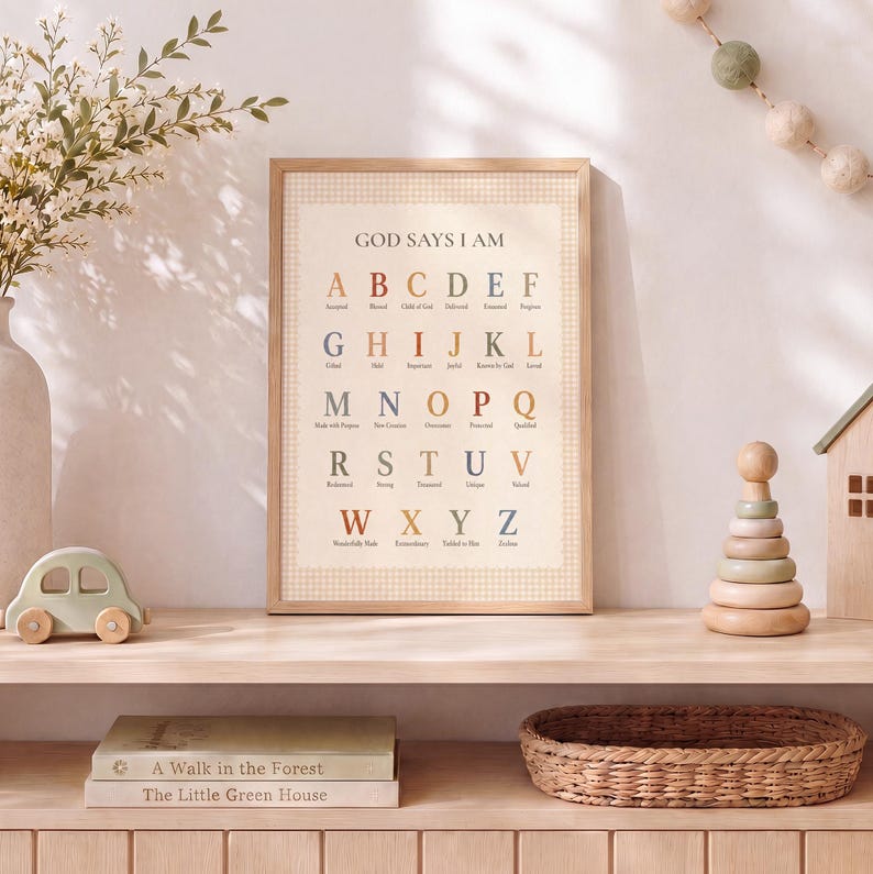 May include: A framed wall art print featuring the alphabet from A to Z in a serif font. Each letter is paired with a descriptive word in a muted color palette. The print has a light beige background with a subtle checkered border and the text GOD SAYS I AM.