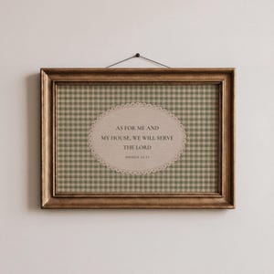 Op de afbeelding: Een ingelijste print met een goudkleurige lijst. De print heeft een groen-wit geruit patroon als achtergrond met een ovaalvormig ontwerp in het midden. De tekst op het ovaal luidt: "AS FOR ME AND MY HOUSE, WE WILL SERVE THE LORD JOSHUA 24:15."