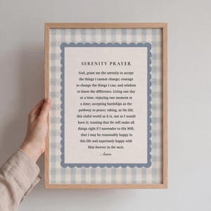 Könnte beinhalten: Ein gerahmter Druck mit dem Serenity Prayer. Der Text ist auf hellem Hintergrund mit blauem Wellenrand zentriert, vor einem blau-weiß karierten Muster. Der Rahmen hat eine helle Holzfarbe.