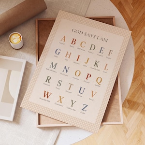 May include: A rectangular wall art print featuring the alphabet from A to Z in a serif font. Each letter is paired with a corresponding word starting with that letter, under the heading GOD SAYS I AM. The design uses a muted color palette.