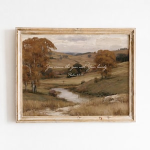 May include: A framed landscape painting featuring rolling hills, a winding stream, and autumn-coloured trees in shades of brown and gold. The text "You crown the year with Your bounty Psalm 65:11" is centred in white cursive script over the scenery.