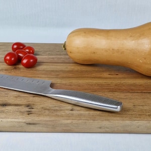 Peut inclure: Une planche à découper en bois avec une courge butternut, un groupe de tomates cerises rouges et un couteau en acier inoxydable. La courge est brun clair, et les tomates sont rouge vif.