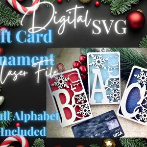 May include: A set of laser cut wooden ornaments shaped like letters of the alphabet, each with a snowman and snowflake design. The ornaments are in red, blue, and green colors. The text "Gift Card" is visible in the image.