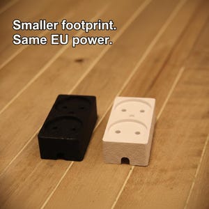 May include: Two EU power outlet adapters, one black and one white, sit on a wooden surface. The black adapter is on the left, and the white adapter is on the right. Text at the top reads: "Smaller footprint. Same EU power."