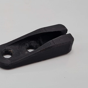 Puede incluir: Pieza de plástico negro impresa en 3D con una ranura y dos agujeros.