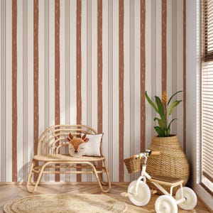 May include: A children's room with striped wallpaper in cream and brown tones. A small, light brown wicker bench holds a deer-shaped pillow. A woven basket holds a plant, and a small tricycle sits nearby. A round, woven rug is on the floor.