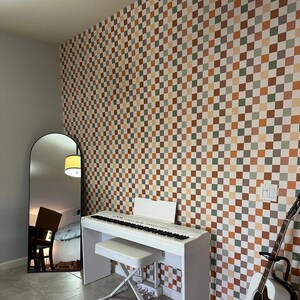May include: A room with a white piano, bench, and acoustic guitar. The wall is covered in a checkered pattern of brown, orange, green, and white squares. A large arched mirror and a yellow lamp are also visible.