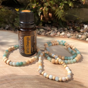 Könnte beinhalten: Eine braune Glasflasche mit Wild Orange ätherischem Öl von doTERRA, mit einem grünen und braunen Perlenarmband auf einer Holzoberfläche.