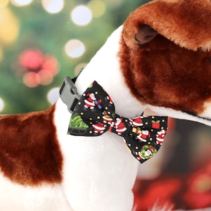 May include: A white and brown dog wearing a black bow tie with a Christmas pattern of Santa Claus, Christmas trees, and presents.