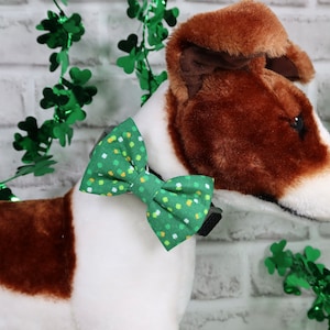 May include: A white and brown stuffed dog wearing a green and yellow shamrock patterned bow tie. The bow tie is attached to a black collar.