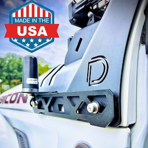 May include: A white vehicle with a black metal roof rack and a Trail Rated badge. The badge is red and black with the words "Trail Rated" and "4x4" in white. The vehicle also has a black antenna and a black side step.