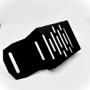 May include: A black metal plate with a series of diagonal and vertical cut-out slots. The plate has a bent, angular shape and appears to be a protective component. The object is set against a plain white background.