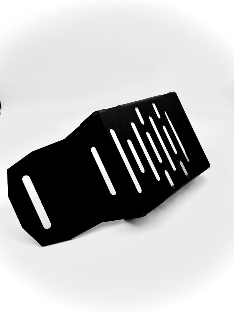 May include: A black metal plate with a series of diagonal and vertical cut-out slots. The plate has a bent, angular shape and appears to be a protective component. The object is set against a plain white background.