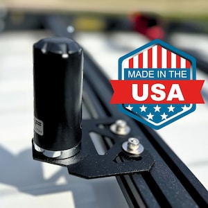 May include: A black metal antenna mount with a black antenna attached to it. The mount is attached to a black metal bar. The antenna mount has a silver screw. The antenna is about 6 inches long. The mount is made in the USA.
