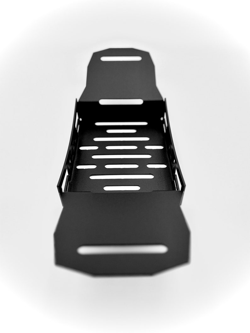 May include: A black metal tray with a rectangular shape and a series of horizontal cut-out slots. The tray has a handle-like design on each end and is set against a white background.