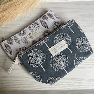 May include: Two small zippered pouches with a white background and black tree and leaf designs. The pouches have a brown label with the text "Natural Style HANDMADE".
