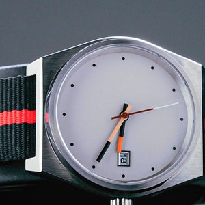 May include: A silver wristwatch with a white face and black and orange hands. The watch has a black and red striped nylon strap.