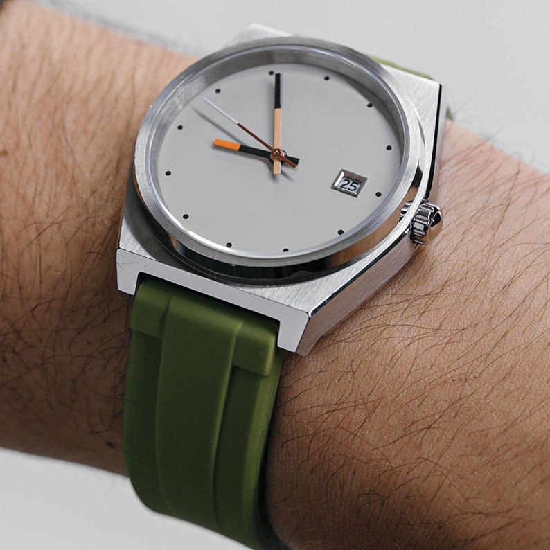 May include: A silver watch with a white face and black hands. The watch has a green rubber strap and a date window that shows the number 25.