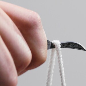May include: A close-up of a hand holding a small, curved, silver tool with a white string attached to the end.
