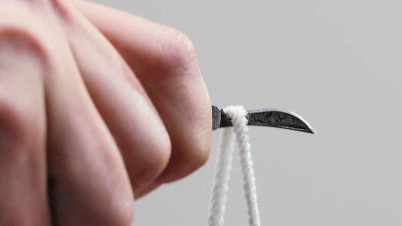 May include: A close-up of a hand holding a small, curved, silver tool with a white string attached to the end.