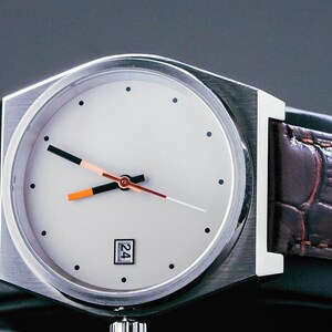 May include: A silver wristwatch with a white face and orange and black hands. The watch has a brown leather strap with a crocodile pattern.