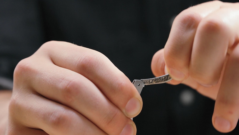 May include: A person's hands are holding a silver folding knife with a textured handle. The knife is being opened.
