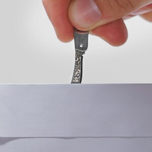 May include: A hand holding a small, silver, pocket knife with a textured blade, about to open a white envelope.