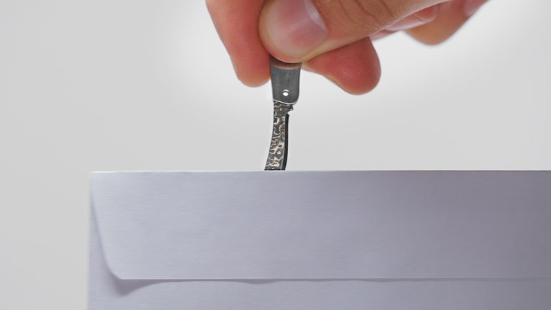 May include: A hand holding a small, silver, pocket knife with a textured blade, about to open a white envelope.