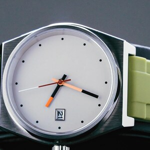 May include: A silver watch with a white face and black hands. The watch has a green rubber strap.
