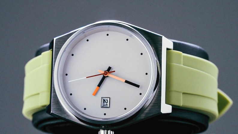 May include: A silver watch with a white face and black hands. The watch has a green rubber strap.