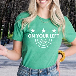 a woman wearing a green t - shirt that says on your left