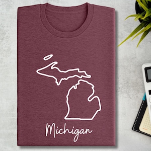 May include: A maroon t-shirt with a white outline of the state of Michigan and the word "Michigan" written below the outline.