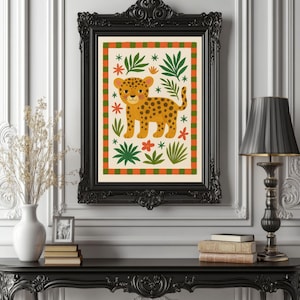 May include: A framed art print featuring a cartoon leopard with a yellow body and black spots. The print has a cream background with green and orange floral and leaf accents. The black frame is ornate.