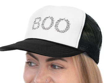 Op de afbeelding: Een zwart-witte truckercap met een wit voorpaneel met daarop het woord "BOO" in zwarte omrande letters. De pet wordt gedragen door een persoon met lang blond haar en een spijkerjack.