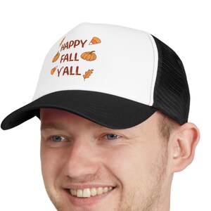 May include: A white and black trucker hat with a black mesh back. The front of the hat has the text "Happy Fall Y'all" in brown lettering with a small pumpkin, leaf, and corncob graphic.