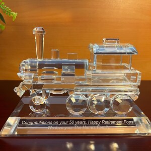 May include: A crystal train engine and boxcar on a clear crystal base. The base has an inscription that reads "Congratulations on your 50 years. Happy Retirement Pops! We love you, The Herres Family."