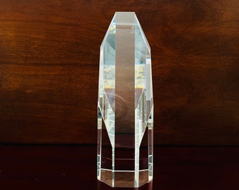 May include: A clear glass award with a faceted design. The award is shaped like a tall, narrow obelisk.