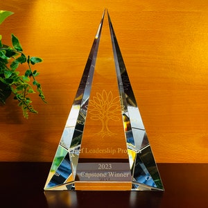 May include: A clear glass pyramid award with the text "Chief Leadership Program 2023 Capstone Winner" engraved on the base.