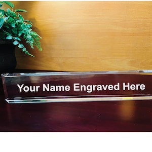 May include: A clear glass desk nameplate with the text "Your Name Engraved Here" in white lettering.
