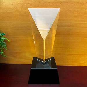 May include: A clear glass award with a black base. The glass is shaped like a pyramid with a pointed top.