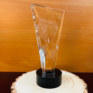 May include: A clear glass award with a black base. The award is shaped like a triangle with a pointed top.