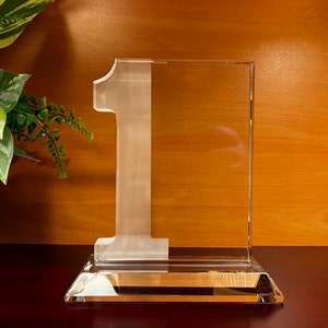 May include: A clear glass award with the number "1" etched into the front. The award has a rectangular base.